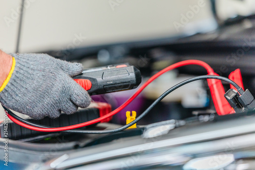 Mechanic using tester to check electric vehicle EV battery voltage under open hood in garage