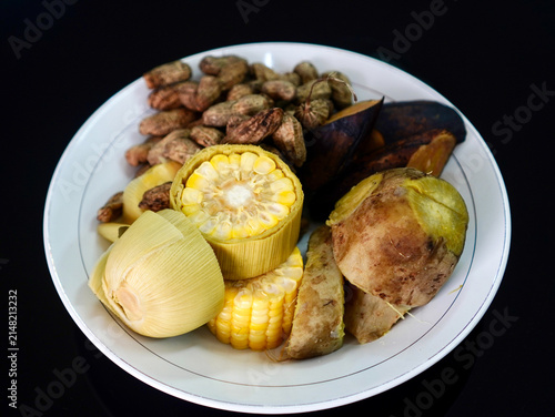 A plate of healthy organic boiled crops featuring boiled peanuts, sweet corn cob, sweet potato, and cooked banana.