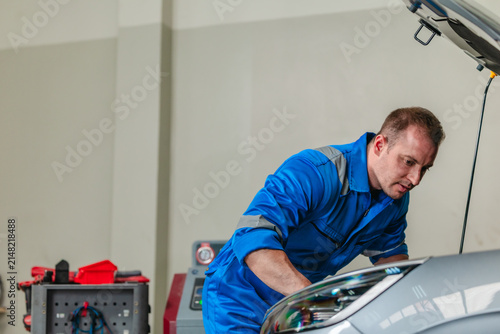 Mechanic using tester to check electric vehicle EV battery voltage under open hood in garage