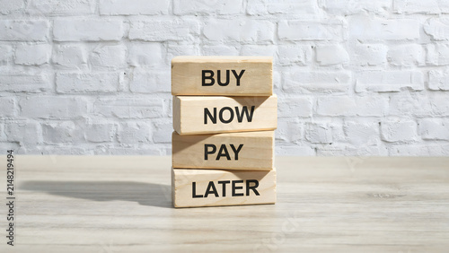A stack of wooden blocks with the words buy now pay later on a table