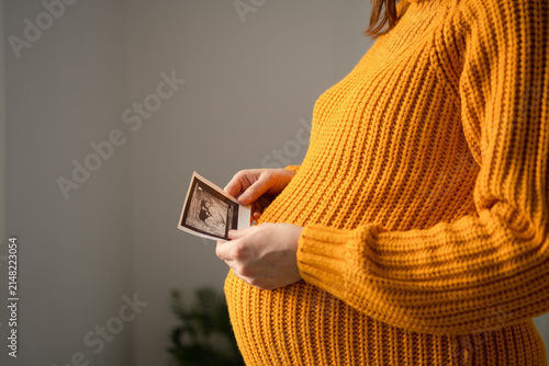 Obraz na płótnie A pregnant woman examines a screening ultrasound photo against a neutral background