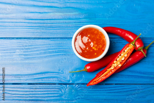 Fotografie Hot chili sauce  in a bowl with fresh red peppers and chili flakes on wooden cutting board