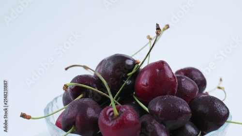 Dark ripe cherries in glass bowl rotate on white background with space for text. Presentation of sweet organic cherry, summer sweet fruit with water drops. Healthy food, snack. 4k 