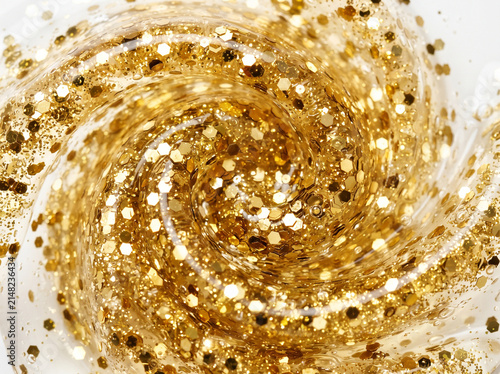 Macro photography of a chemical reaction: a swirling vortex of golden glitter and precipitate microparticles in a transparent liquid.