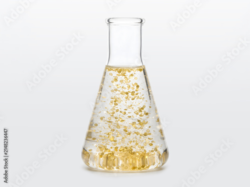 Chemical experiment in a flask: golden particles and glitter precipitate in a transparent solution.
