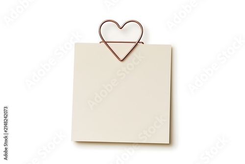A blank creamcolored square note held by a rose gold heartshaped paperclip, isolated on a white background