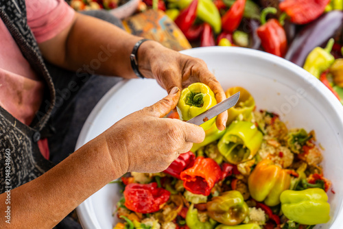 Close-up of hands coring fresh green peppers with a knife over a bowl of colorful peppers during traditional food preparation, rustic kitchen workflow, natural light, vibrant produce.