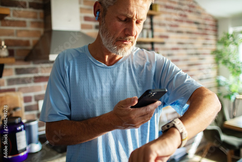 Active senior man checking smartwatch and phone in home kitchen