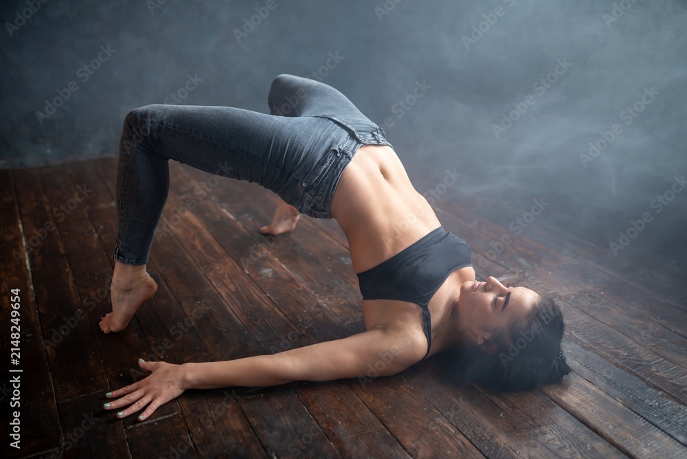 Obraz premium Athletic woman doing a bridge pose variation in smoke