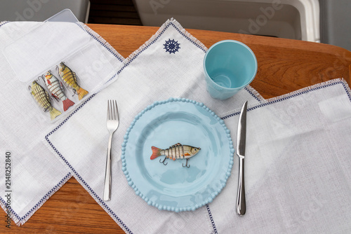Fishing lures on a plate with a fork and knife. Humorous concept of a fishing failure.	
