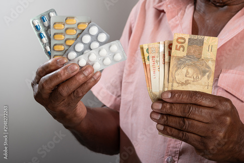 Quadro su tela Elderly man holding medication and Brazilian currency