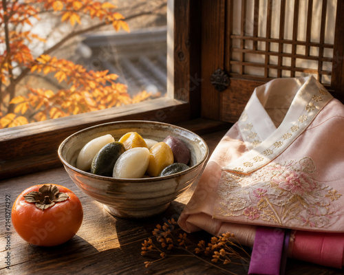 chuseok. Songpyeon rice cakes, persimmon and hanbok fabric on windowsill, Korean harvest celebration concept, representing seasonal cycles and harvest abundance.