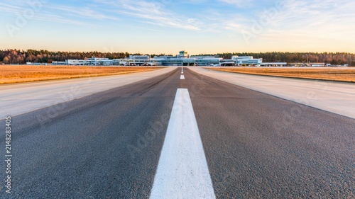 Long airport runway stretching toward the horizon under a bright blue sky, featuring strong perspective, clean pavement and central markings, ideal for aviation, travel and transportation concepts.
