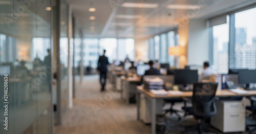 A modern office environment featuring desks with computers and employees. The blurred perspective adds depth to the busy workplace atmosphere.
