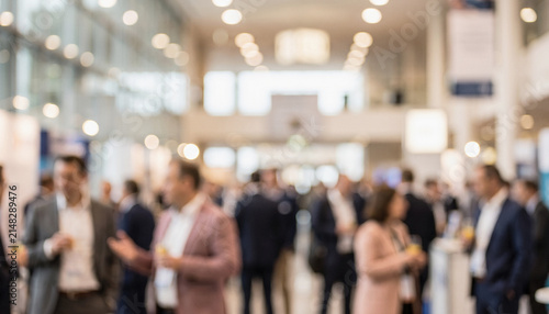 A blurred image of a busy conference or networking event, showcasing a diverse group of professionals engaging in conversation and sharing experiences.