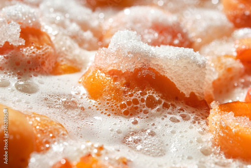 Cooking apricot jam with sugar and foam. Orange color apricot berries bubbling in a pot during the simmering process for a fresh homemade confiture. High sugar consumption. Shallow depth of field. 