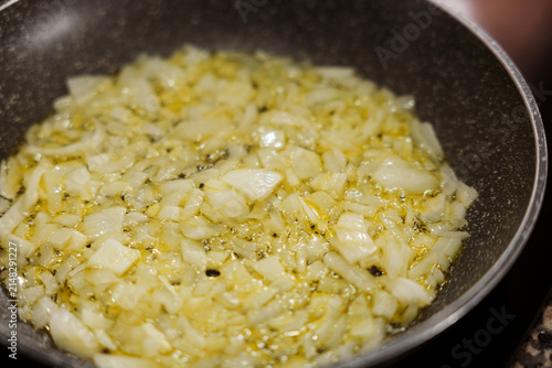 Diced onions sauteing in olive oil in frying pan closeup.