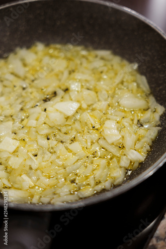 Diced onions sauteing in olive oil in frying pan closeup.