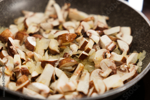 Sliced mushrooms and onions sauteing in frying pan on stove.