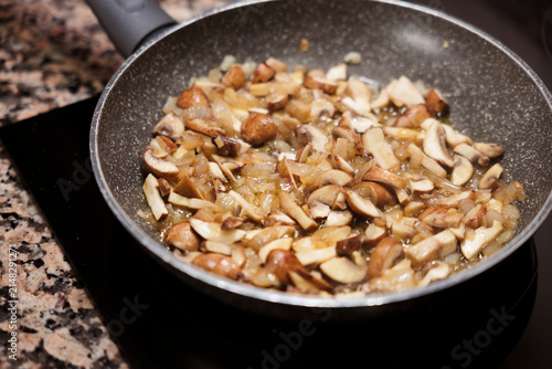 Sliced mushrooms and onions sauteing in frying pan on stove.