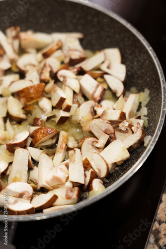 Sliced mushrooms and onions sauteing in frying pan on stove.