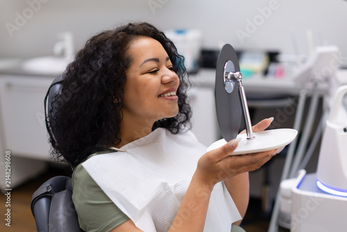 Foto Happy black female patient smiling while checking her new smile in a handheld mi