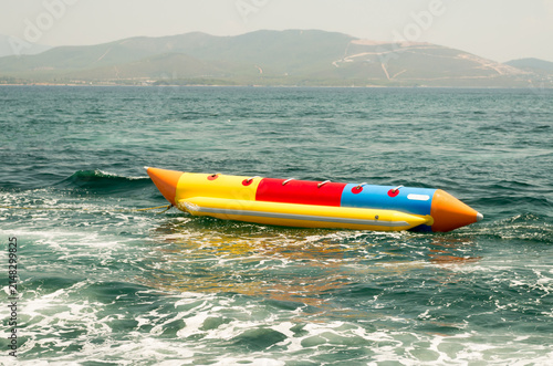 Colorful inflatable banana boat water sled floating on sea waves at a summer beach resort close up.