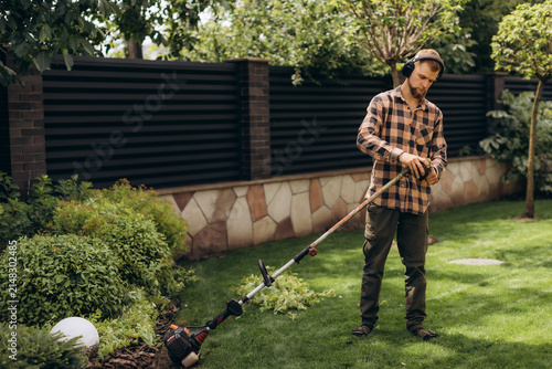 Gardener trimming lawn with string trimmer in backyard