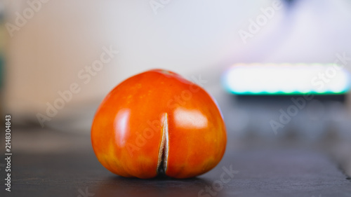 Ugly ripe red tomato with funny unusual split shape on dark slate board, imperfect organic fresh vegetable for food waste prevention concept, healthy homegrown agriculture design backdrop.