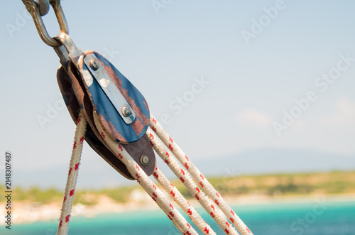 Vintage sailboat pulley block with marine rigging ropes over a blurred turquoise sea coast background close up.