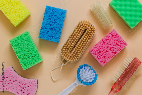 Assortment of colorful cleaning sponges and scrub brushes arranged on a beige background with copy space, representing household cleaning, hygiene, and home maintenance.