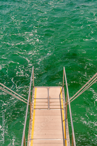 Emerald green ocean water background with an empty boat ladder and text copy space for summer travel design.