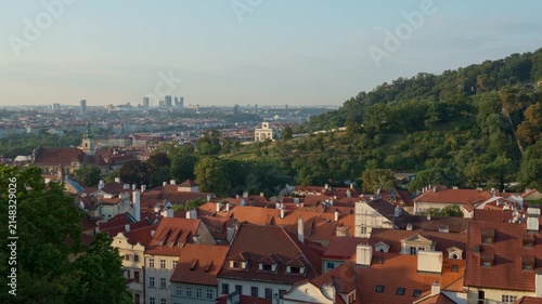 Prague city panorama showcases historic houses near green Petrin Hill. Old town architecture contrasts with distant modern skyscrapers at morning. Czechia landmark offers travel scenery.