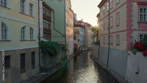 Historic Certovka canal flows between colorful old buildings in Prague. Warm morning sunlight shines through ancient stone facades along the European urban waterway. Scenic tourism view.