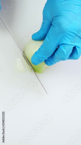 Professional chef hands in blue gloves slicing half onion close up on white kitchen cutting board. Minced with big iron knife. Cooking, preparing ingredients in restaurant. Top down view. 4k footage.