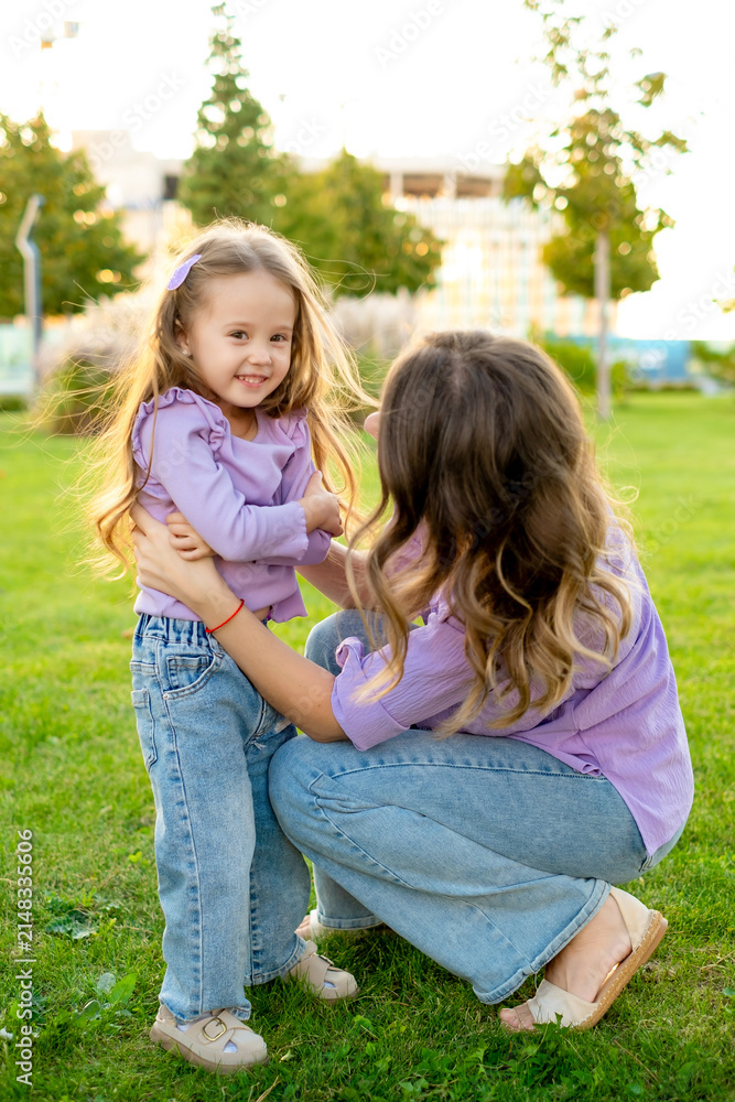 Fototapeta premium mother and child walking in the park in the summer, having fun together, mother and daughter hugging and kissing on a green lawn, motherly love