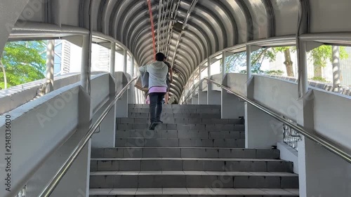 Daily commuters walking through modern pedestrian link bridge at KTM railway station in Kuala Lumpur city center.