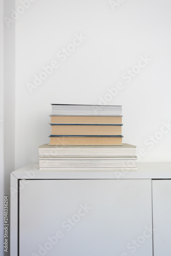 Stack of hardcover books on white cabinet in minimalist home interior with copy space. Education, reading, learning, knowledge, home library, and modern lifestyle.