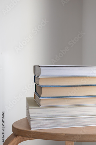 Stack of books on wooden side table in minimalist interior. Education, reading, learning, knowledge, and modern lifestyle, book club