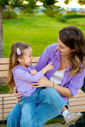 mother and child walking in the park in the summer, having fun together, mother and daughter hugging and kissing on a green lawn, motherly love