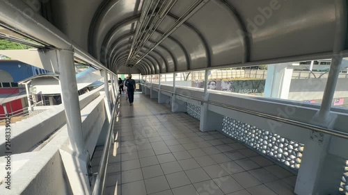 Daily commuters walking through modern pedestrian link bridge at KTM railway station in Kuala Lumpur city center.