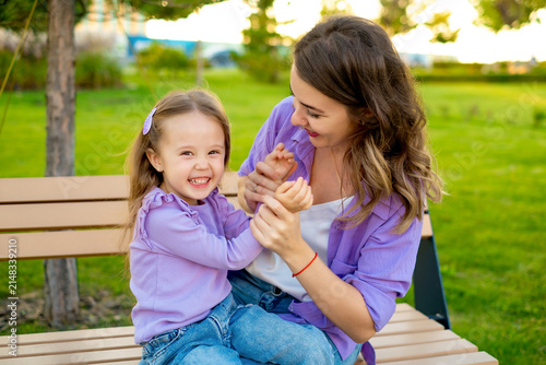 mother and child walking in the park in the summer, having fun together, mother and daughter hugging and kissing on a green lawn, motherly love