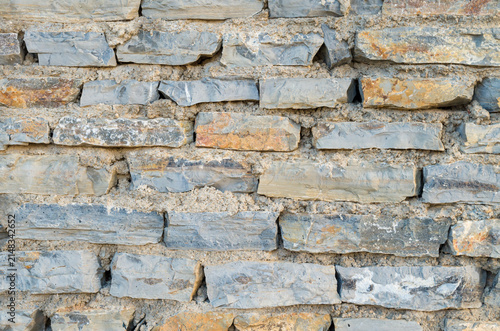 Abstract architectural background of a rustic stone wall texture with gray and orange brick shaped natural stones close up.