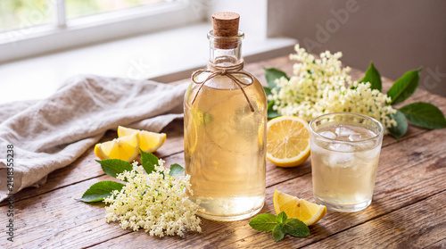 Elderflower cordial in glass bottle with lemon and flowers on table  