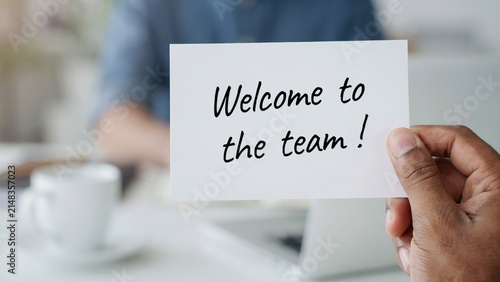 Hand holding a white card with the handwritten text welcome to the team