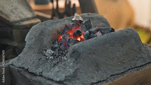 A blacksmith works at an anvil, heating metal in a forge. The glowing coals and tools surround the craftsman, showing the skill involved in metalworking
