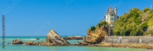 Panoramic view showing sea rocks and the historic Villa Belza set against a clear blue sky on the Basque coastline in Biarritz, France