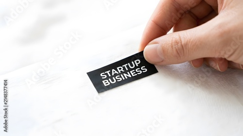 Hand placing small sticker with words startup business on fabric.