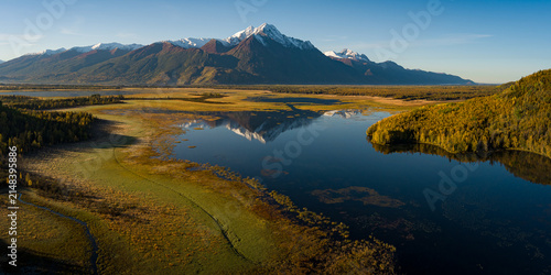 Alaskan snow-capped mountains in distance during fall with rising sun on the valley and lake reflection