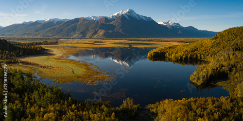 Alaskan snow-capped mountains in distance during fall with rising sun on the valley and lake reflection